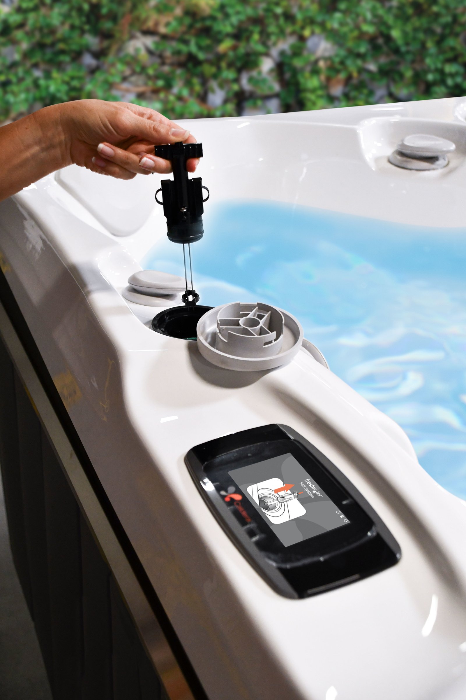 Hand dropping a FreshWater Salt System titanium cartridge into the port of a Caldera spa, guided by the control panel
