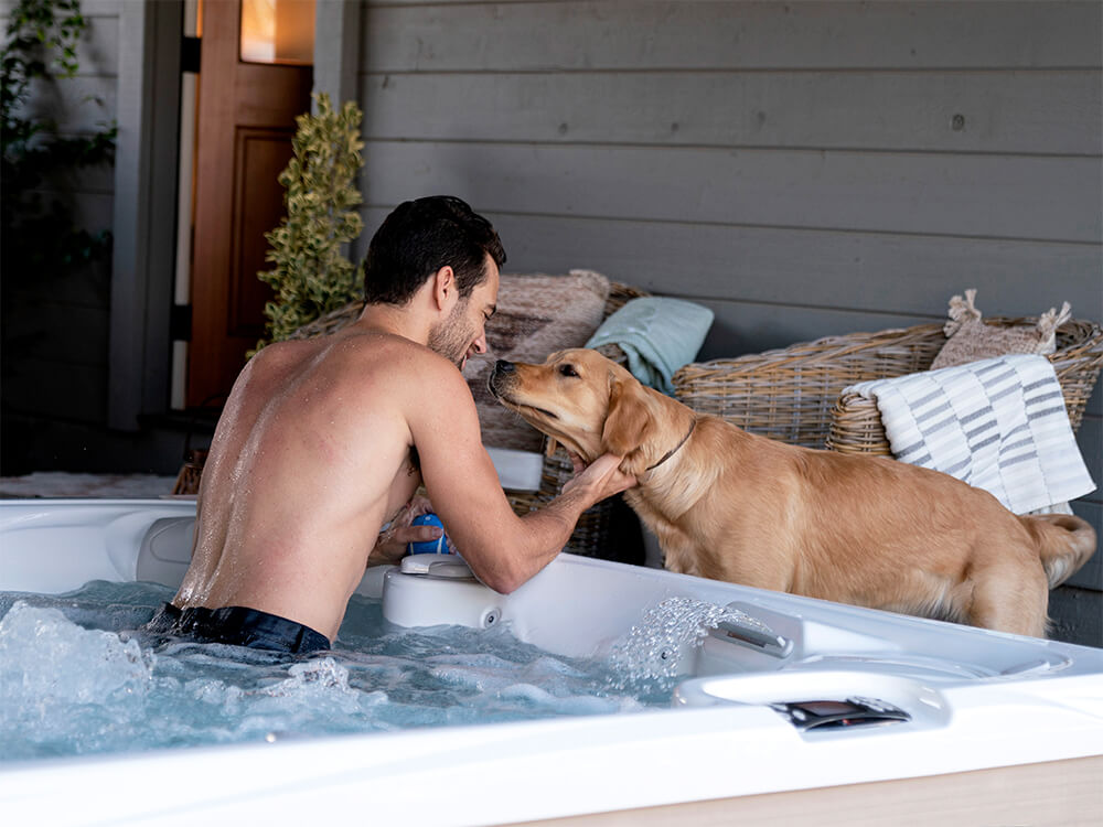 A man relaxing in a Caldera Paradise Reunion spa with his dog beside it