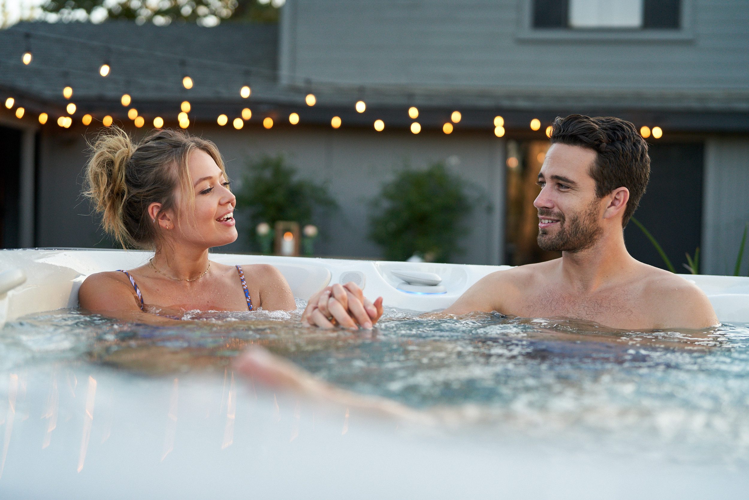 Couple holding hands in a Caldera Utopia Geneva hot tub under string lights