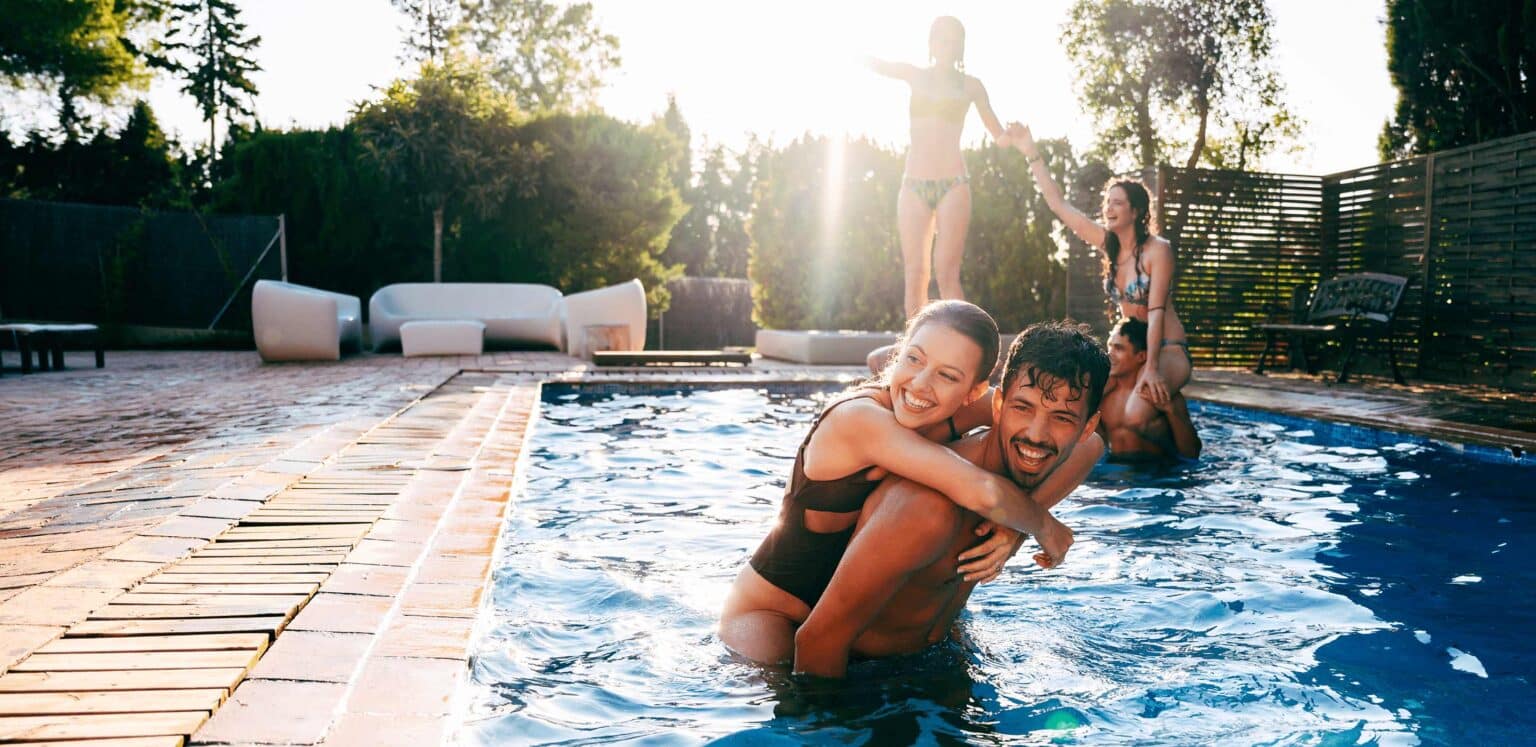 Friends laughing together in a backyard fiberglass pool on a sunny day