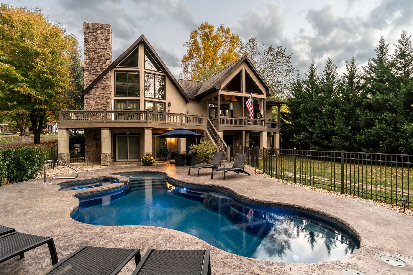 Freeform fiberglass pool behind a timber-frame home surrounded by evergreens