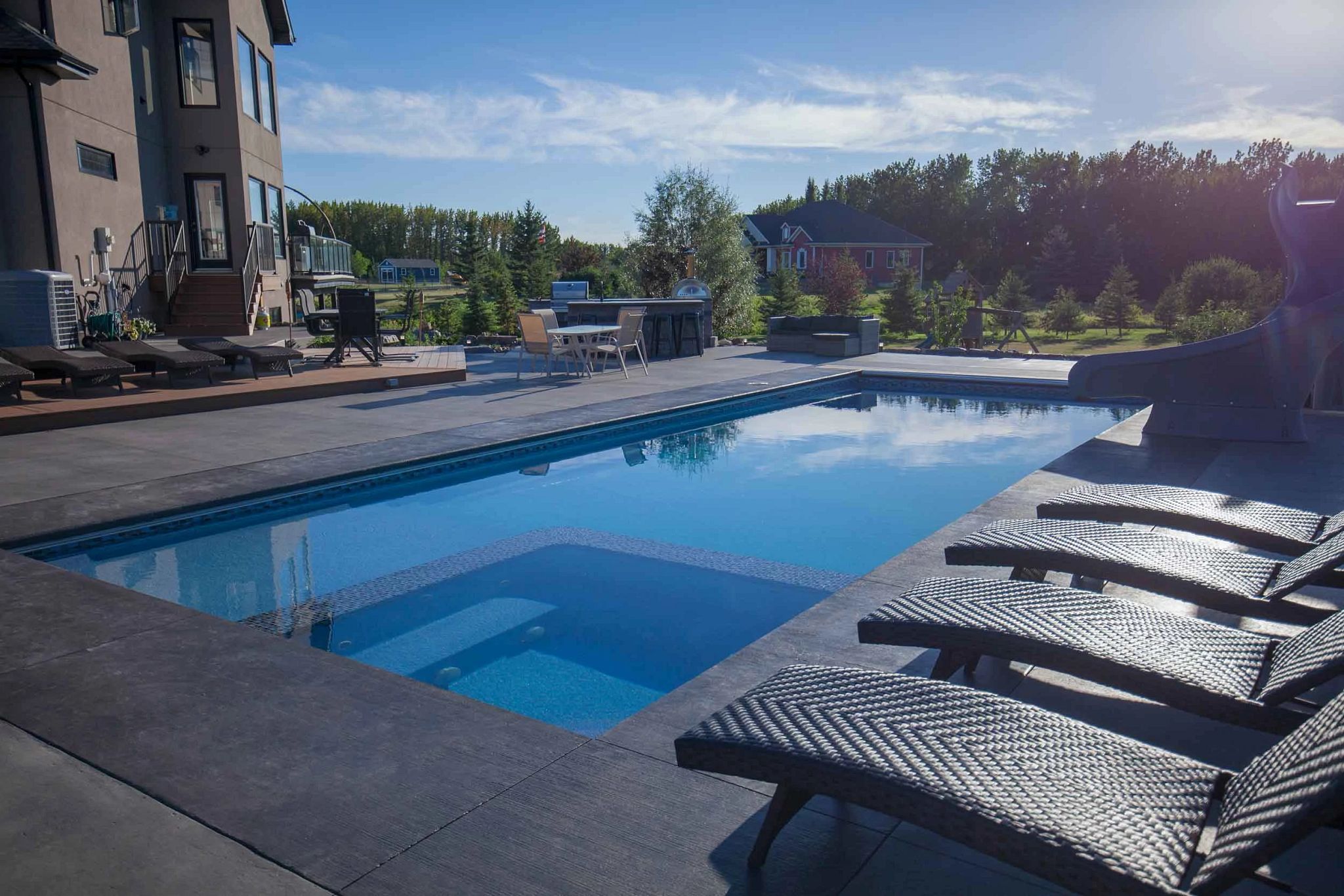 Fiberglass inground pool with a tanning ledge and lounge chairs on a dark stone deck