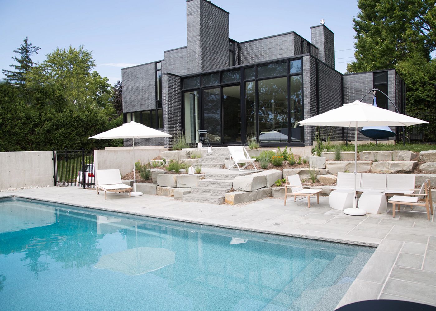 Rectangular fiberglass pool beside a modern glass house with umbrellas and lounge chairs
