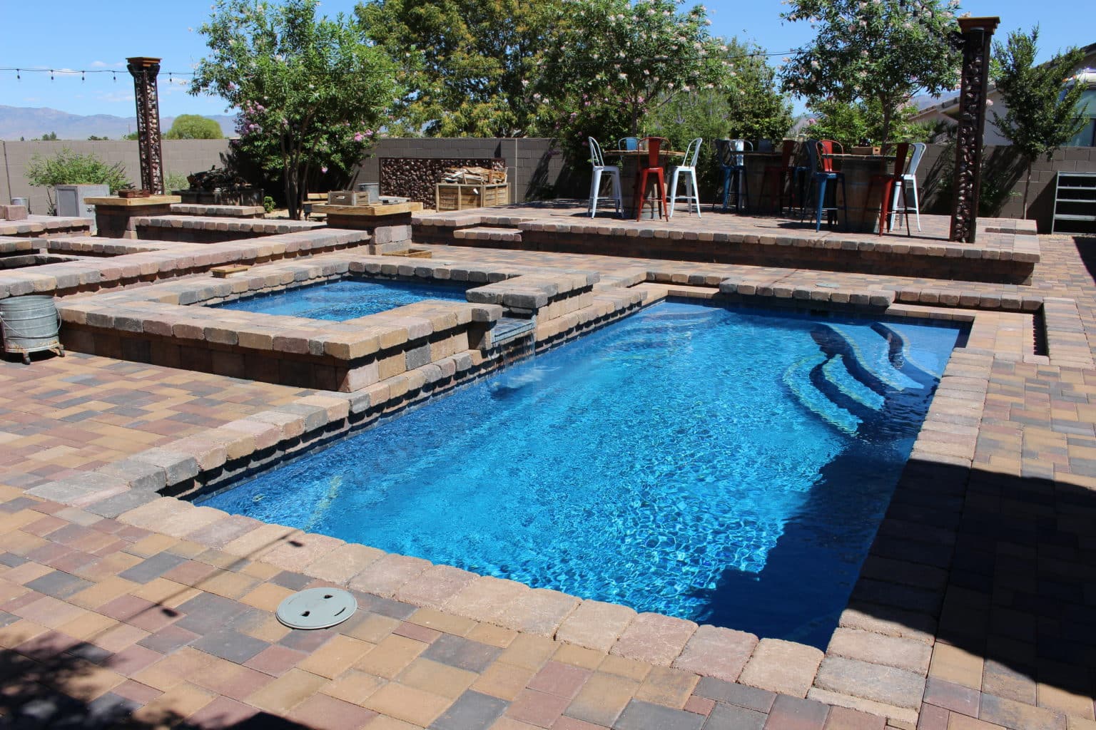 Fiberglass pool with entry steps set into a paver patio beside a raised spa